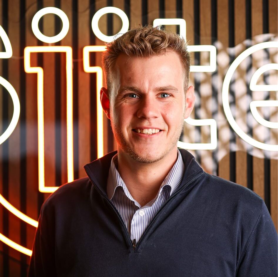 Man smiling in front of neon sign.