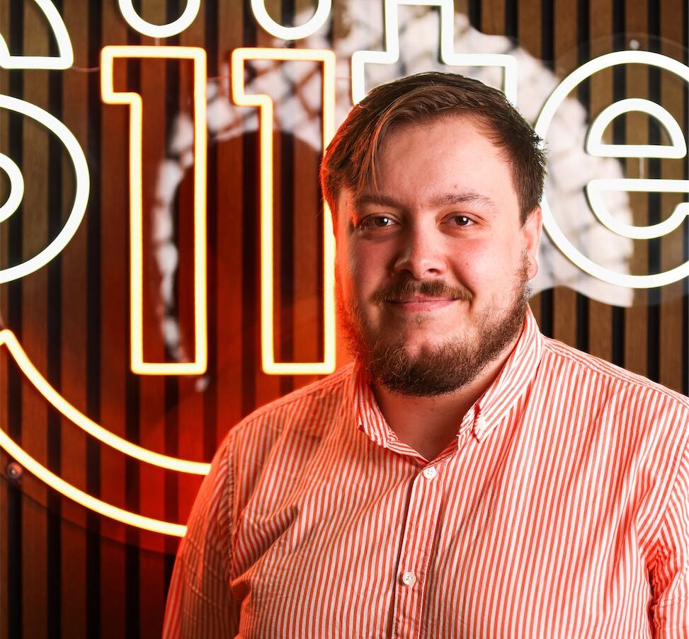 Man smiling in front of neon sign.