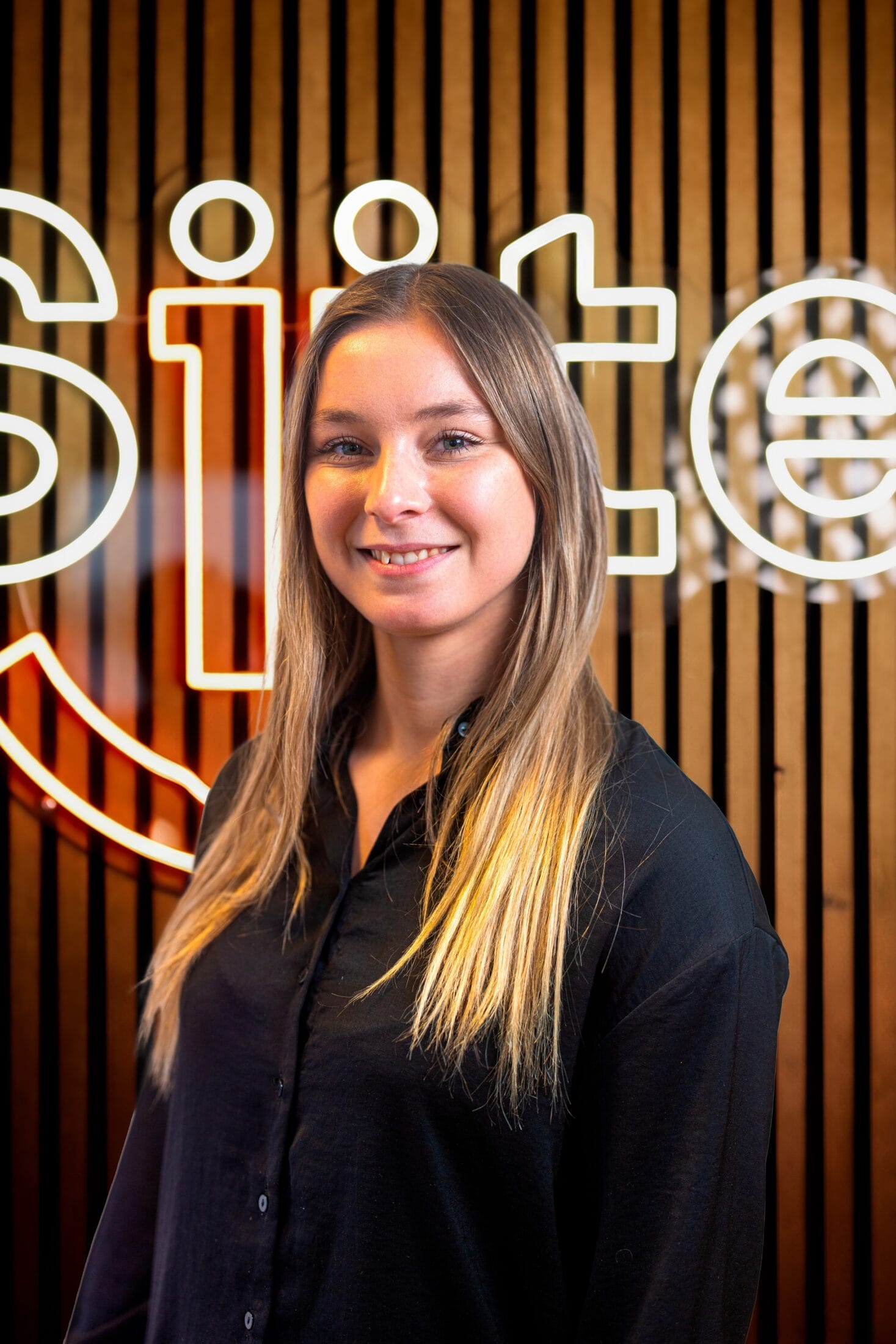 Woman smiling in front of illuminated sign.