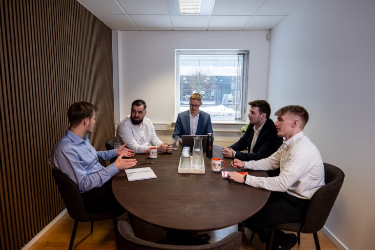 Fem mænd ved mødebord diskuterer